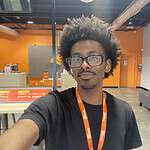 Person with glasses and afro in bookstore with orange walls.