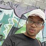 Person wearing a black T-shirt with support for Black Trans Lives and a beige cap.