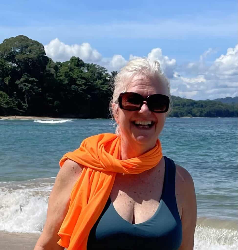 Smiling woman with sunglasses and orange scarf at the beach.