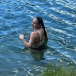 Woman in red swimsuit relaxing in lake water near grassy shore.