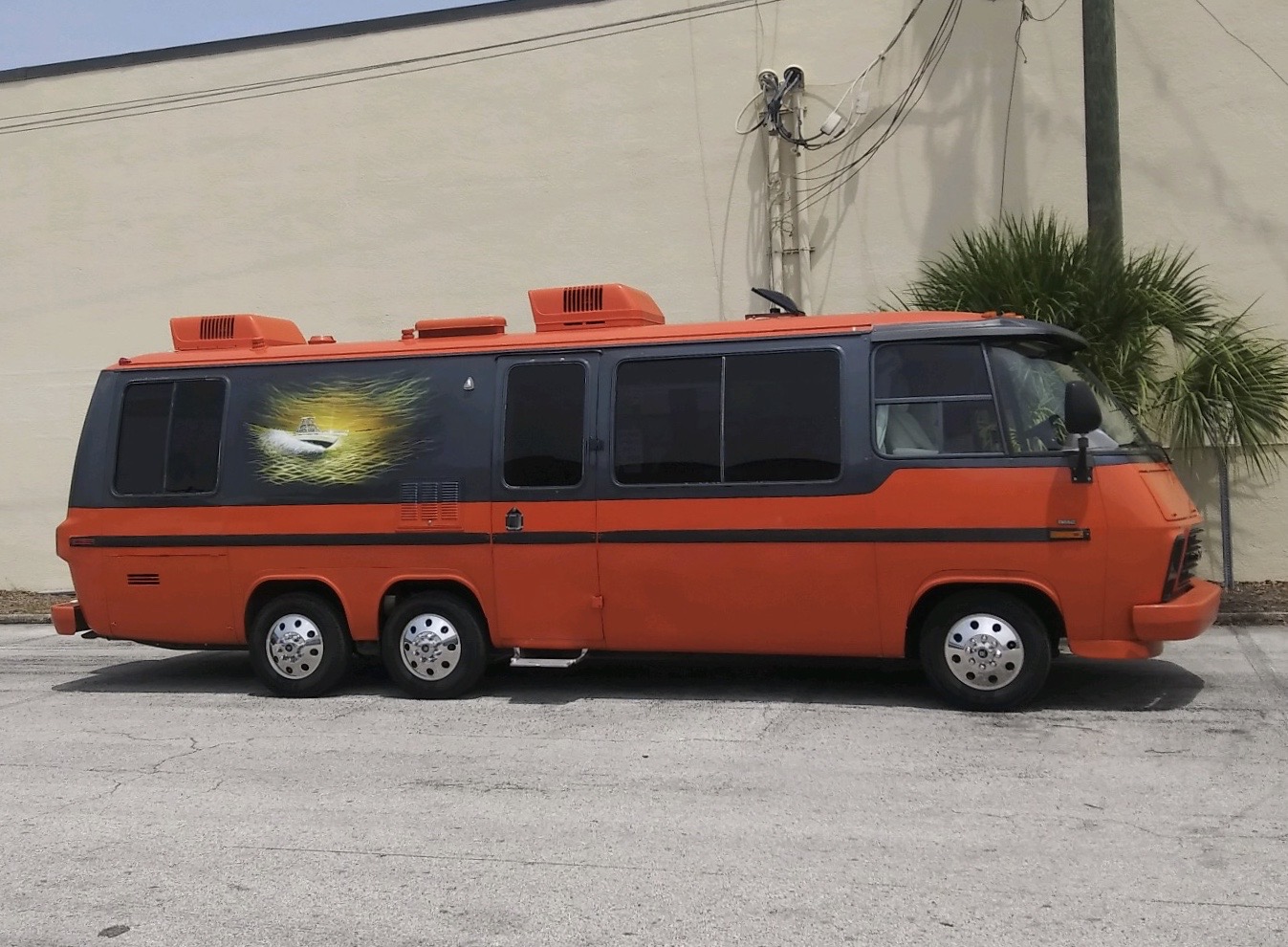 Orange bus with a space-themed mural parked on street.