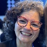 Smiling woman with curly hair and colorful glasses at community event.