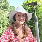Woman with wide-brimmed hat smiling in community garden with gardening tools.