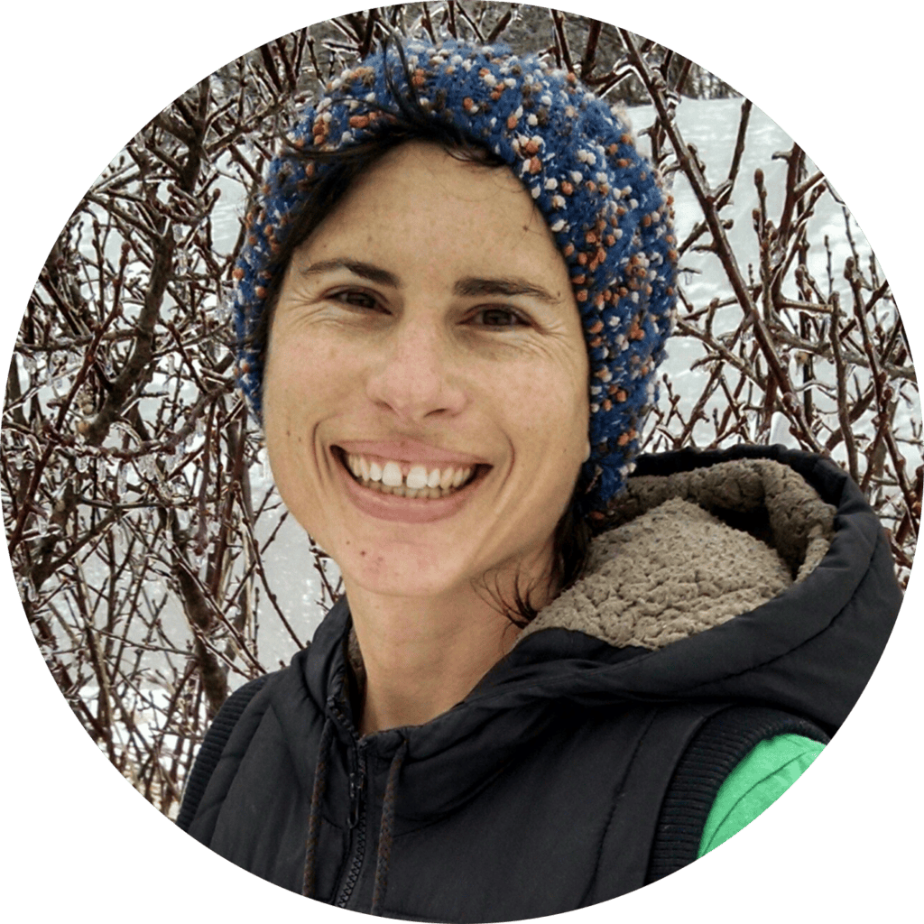 Woman smiling outdoors in winter with snow-covered branches behind her.